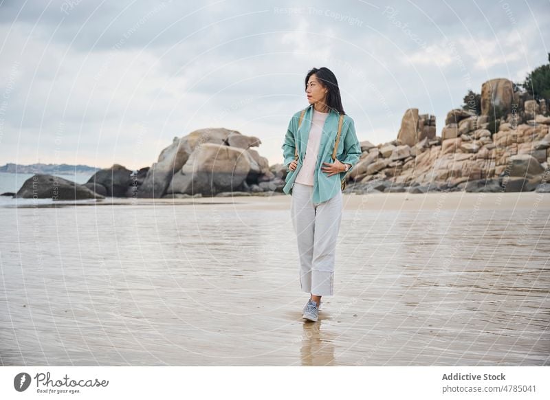 Beautiful Asian girl walking on the beach in Autumn during her trip nature rocks cloudy sand wet wet sand Chinese girl woman one person people portrait winter