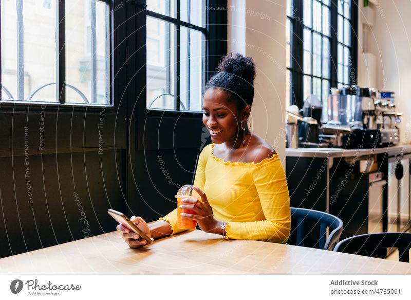 Happy woman using phone and drinking juice in cafe smartphone relax happy young cup mobile female african american black beautiful connection device cheerful