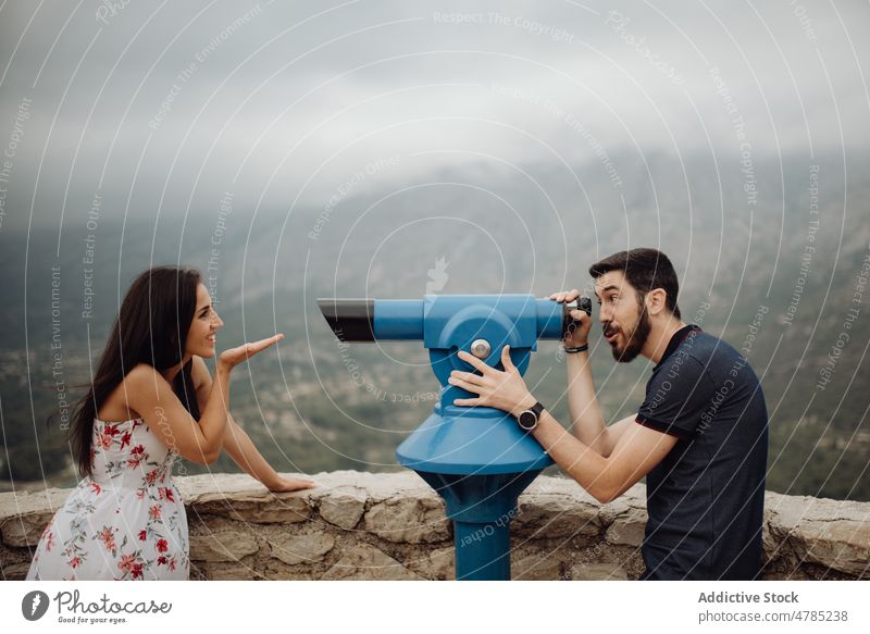 Cheerful couple having fun with binocular on town observation deck mountain cheerful playful playing joyful explore casual viewpoint countryside valley foggy