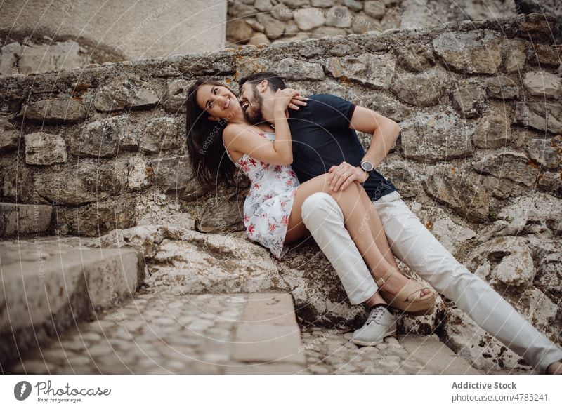 Happy couple having fun while sitting on stone street kiss town love happy romantic affection playful casual embrace cuddle cobbled summer rural young adult