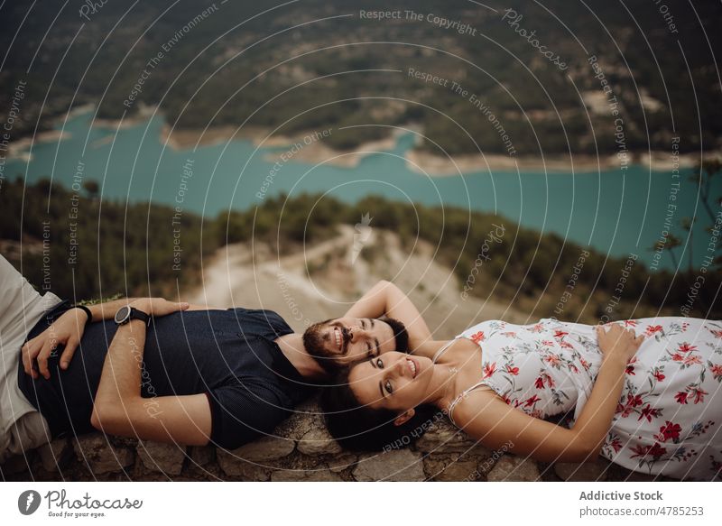 Affectionate couple resting while lying on stone fence in mountains valley love observation deck travel affectionate sensual tender casual parapet viewpoint