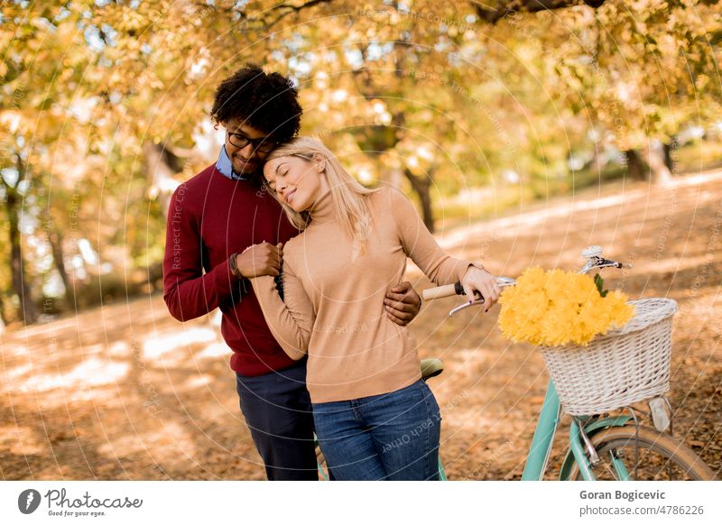 Multiracial couple with bicycle in the autumn park foliage fall flowers yellow man woman young multiethnic happy leisure caucasian smiling together love outside