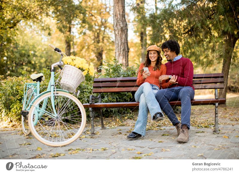 Multiratial loving couple sitting on bench in the autumn park african american attractive basket bicycle caucasian dating fall flowers friends happiness happy