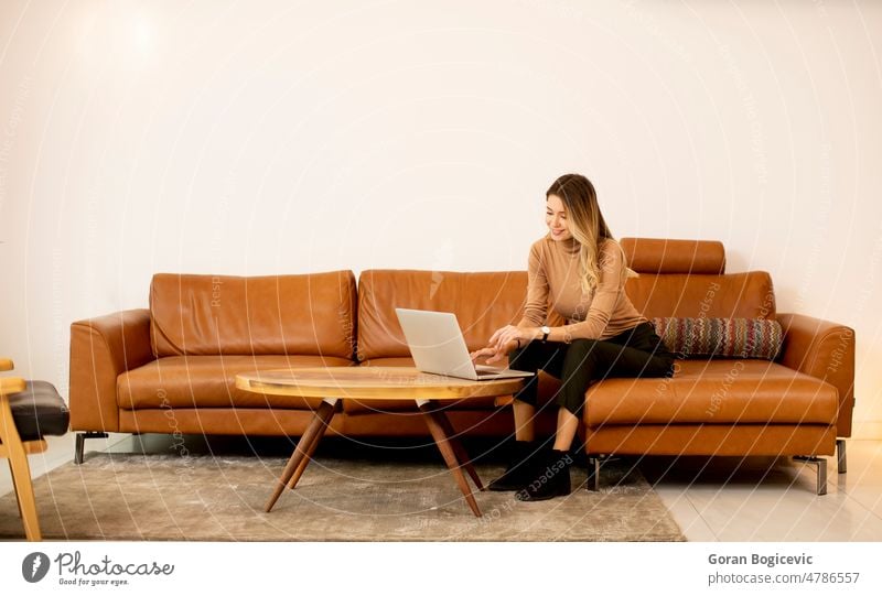 Young beautiful woman using a laptop at home alone attractive beauty blonde brunette calm casual caucasian comfortable communication computer couch cute female