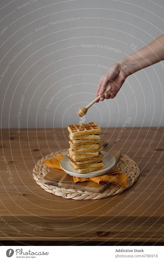 Anonymous person using dipper with syrup on delicious waffles served on ceramic plate dessert sweet homemade food baked culinary tasty eat yummy pile appetizing