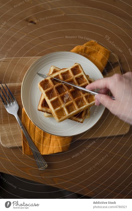 Anonymous person eating delicious waffles served on ceramic plate dessert sweet homemade food baked culinary tasty yummy pile fork appetizing table kitchen