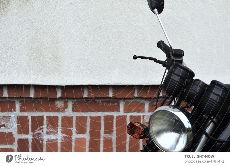 Restored vintage DDR motorcycle MZ (detail) with lamp, turn signals, speedometer, handlebar, handlebar grip, rear view mirror stands in front of a bright house facade with bricks