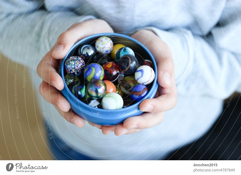 A child holds a bowl with colorful marbles Marbles Child Infancy Playing fun Boy (child) Leisure and hobbies Children's game muck about Colour photo Human being