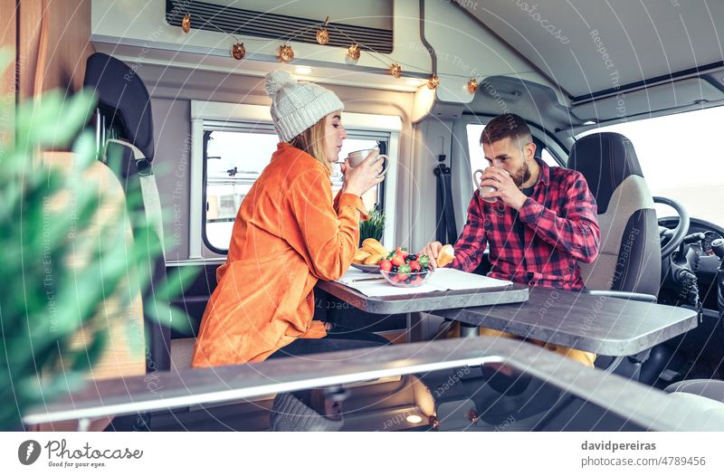 Friends having breakfast in a camper van motorhome friends man woman drinking cup coffee morning bun eating fruit healthy blueberry strawberry picking vacation