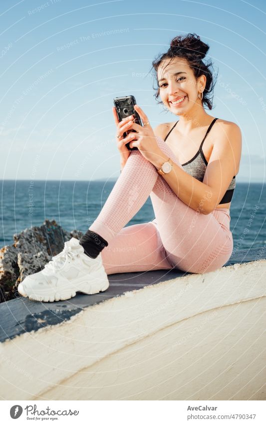 Close up image of Young woman checks her phone after a day training outdoors. Checking social media and posting new images to her fans. Famous athletes and body summer good looking concept.