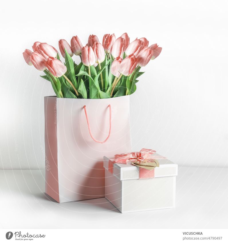 Beautiful pink tulips flowers bouquet in shopping bag and gift box with ribbon at white background. beautiful greeting setting front view birthday