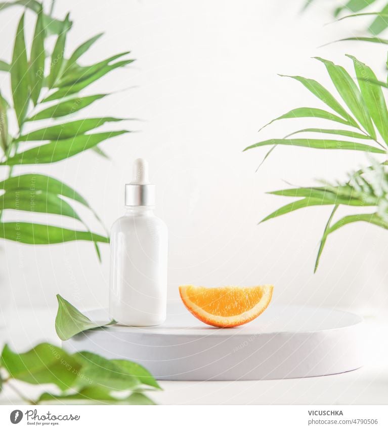 Cosmetic pipette bottle and orange slice on podium at white showcase background with green tropical leaves. cosmetic beauty product vitamin c serum modern
