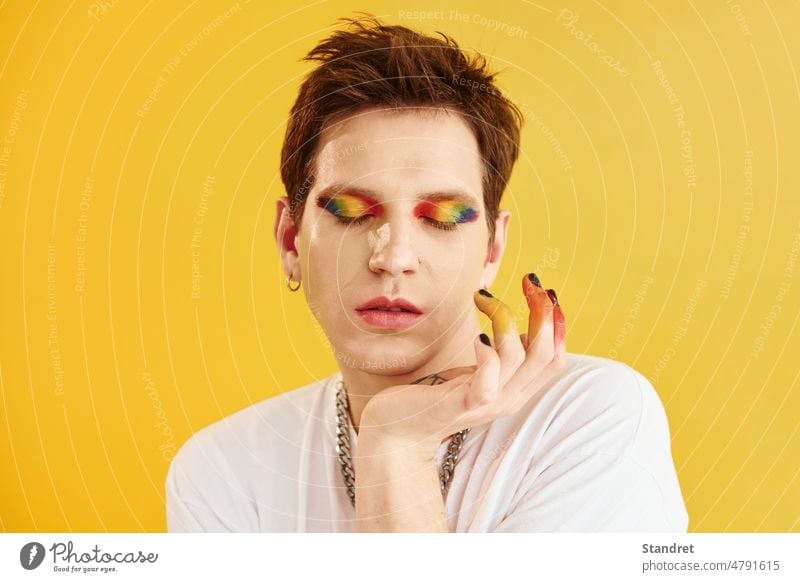 Young gay man is standing in the studio and posing for a camera. Rainbow make up young portrait face gender lgbt makeup guy transgender androgynous yellow
