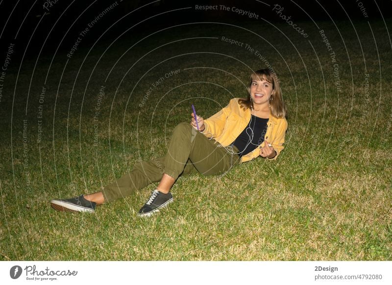 woman sitting on grass in a park at night using mobile phone young female 1 beautiful attractive pretty happy girl outdoor person lifestyle portrait happiness