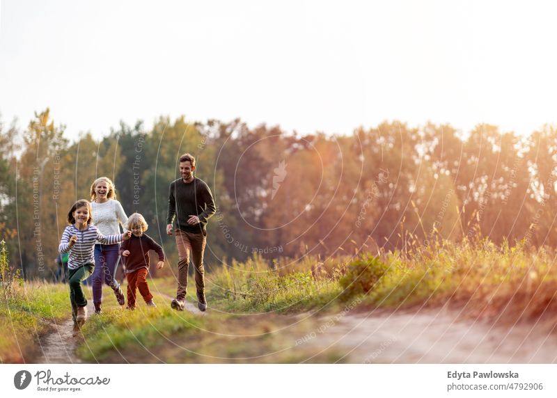 Young family having fun outdoors walking running leaf nature field park autumn fall man dad father woman female mother parents relatives son boy kids children