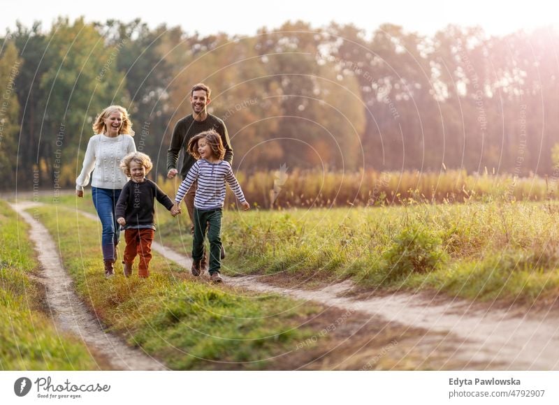 Young family having fun outdoors walking running leaf nature field park autumn fall man dad father woman female mother parents relatives son boy kids children