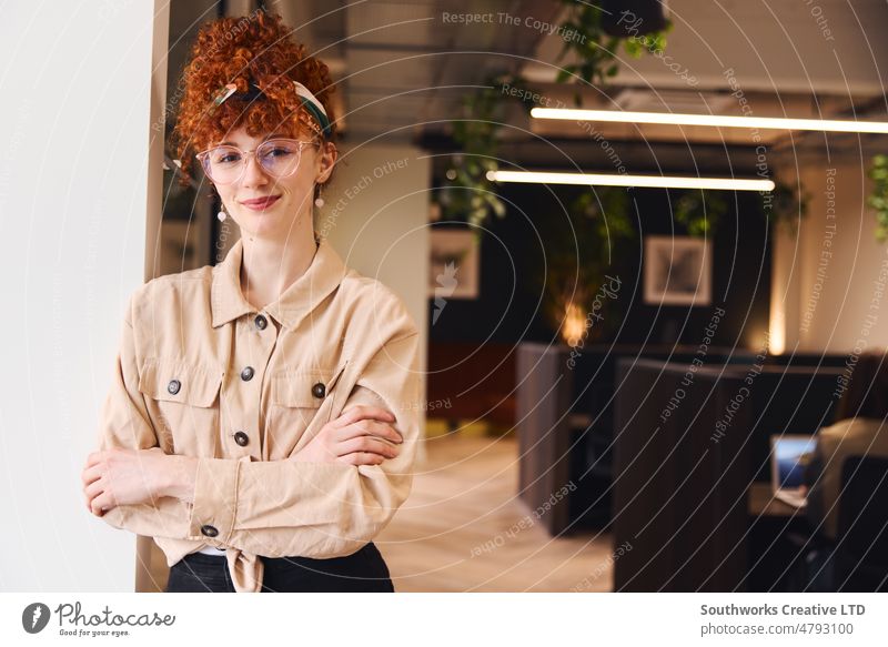 Portrait of confident young white woman with red curly hair wearing glasses, smiling and looking at camera in coworking space portrait eyeglasses smile office