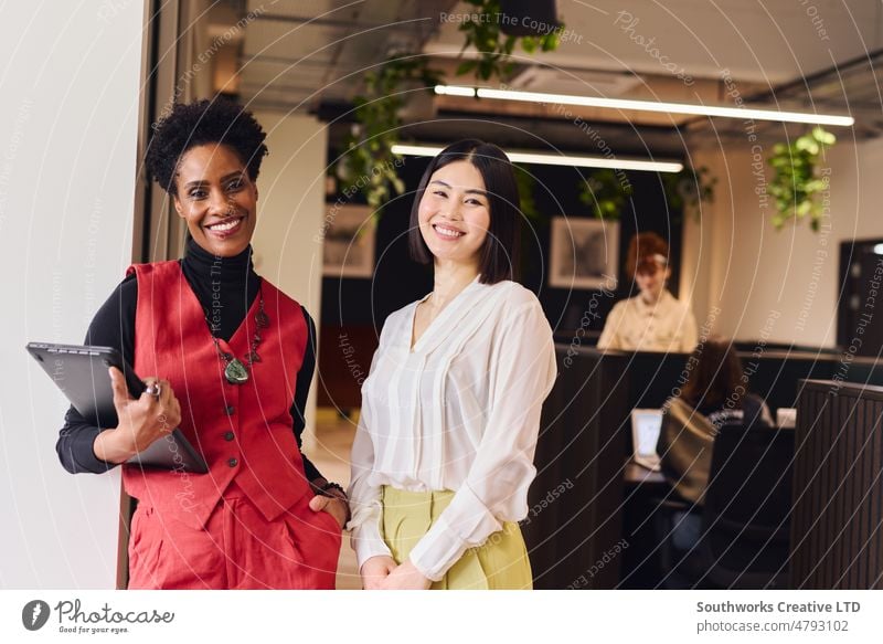 Portrait of cheerful mature black woman and mid adult Chinese female colleague in open plan office space smiling portrait chinese smile look coworking indoors