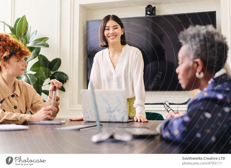 Portrait of Chinese mid adult businesswoman with laptop smiling and listening to female colleagues in boardroom portrait chinese meeting smile discuss