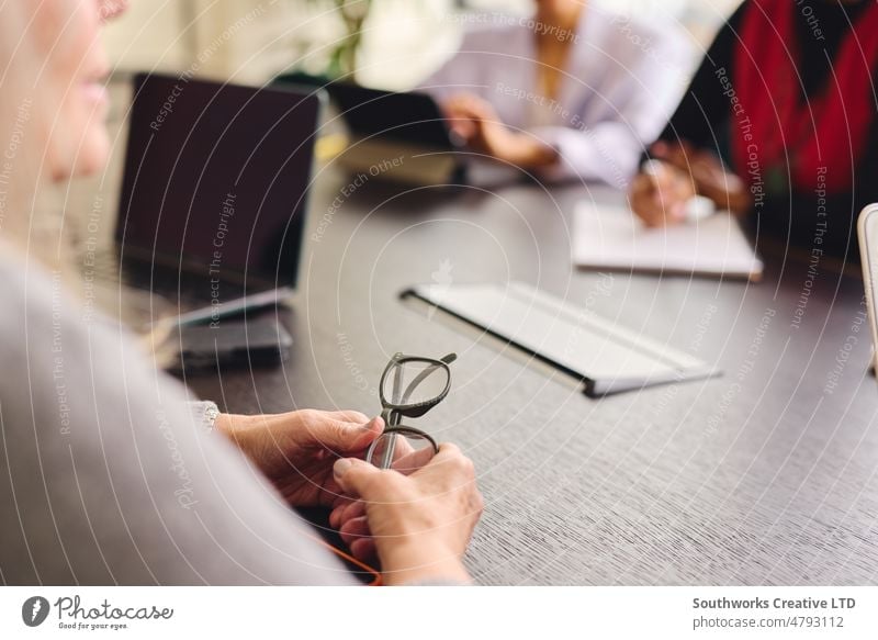Close up of woman holding glasses with hands resting on meeting table with female colleagues in background closeup businesswoman eyeglasses discuss boardroom