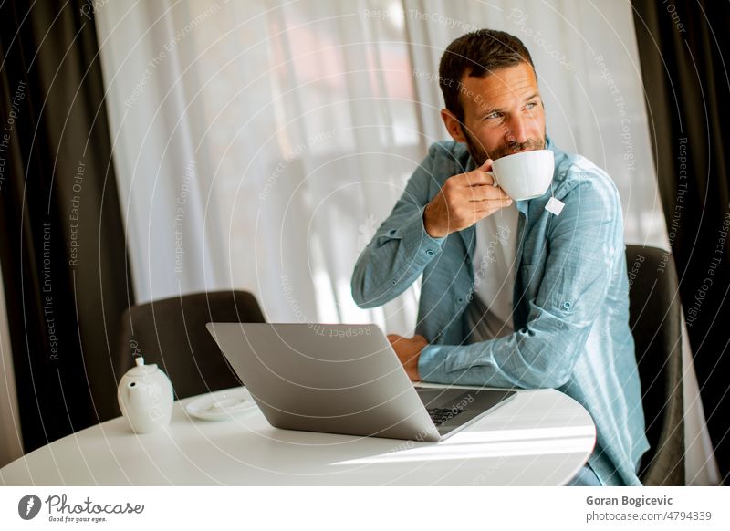 Young man using laptop and drink tea in the living room lifestyle cup office computer modern business technology entrepreneur job internet person adult male mug