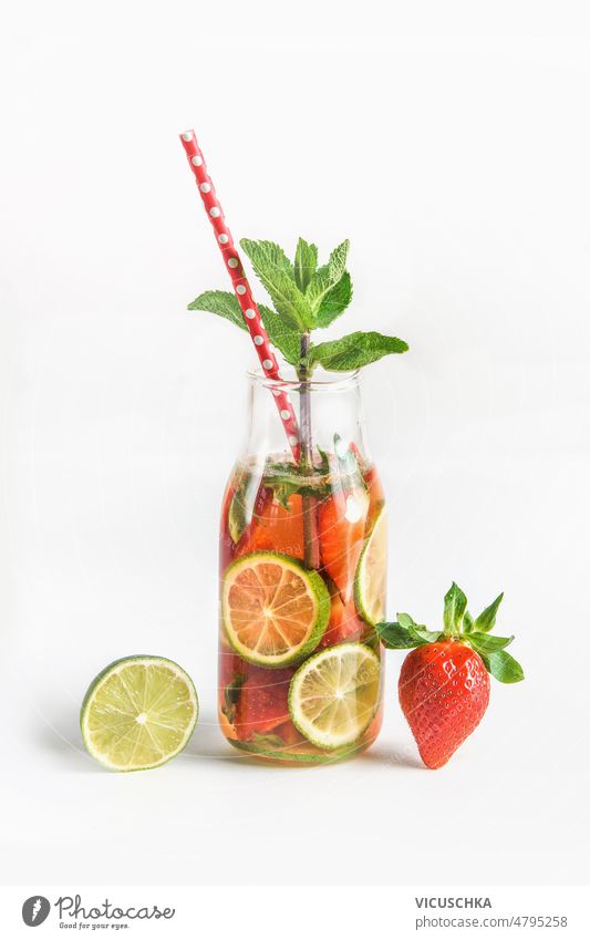 Tasty infused water in bottle with drinking straw and ingredients: lime, strawberry and mint leaves at white background tasty summer refreshing drink fruits