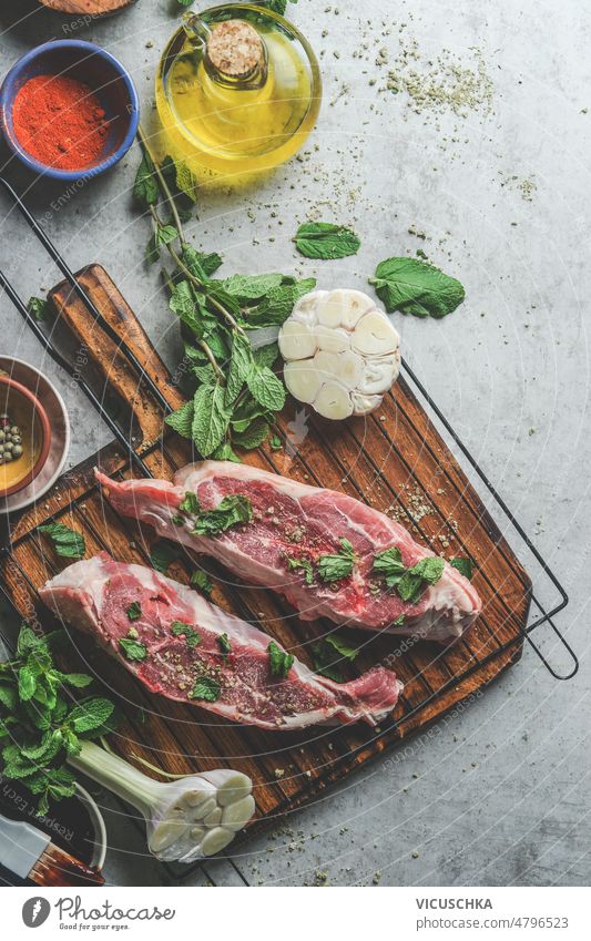 Raw lamb meat with cooking ingredients: olive oil, mint leaves, garlic on wooden cutting board cooking preparation raw grey concrete kitchen table spices herbs