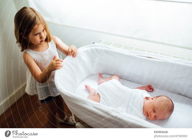 Older sister and little newborn brother in the crib. Managing jealousy between siblings managing brothers angry horizontal indoor infant emotion son conflict