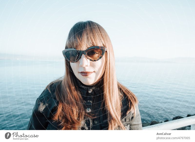 Modern young woman using sunglasses during a sunny summer day with half smile looking to camera. All black wear on hot days. Holidays on the mediterranean sea for nordic people concept.