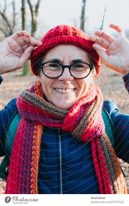 Frontal portrait of an old woman smiling to camera using glasses and putting on a cap for the cold and winter.. Aging well and healthy concept, family grandmother image. Active third age concept