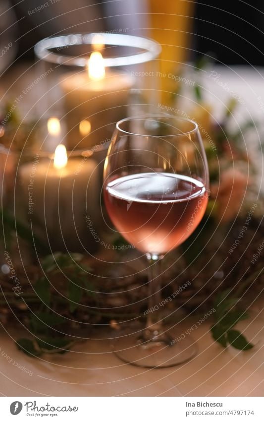 A misted wine glass half full of rosé wine in front of two lit candles on blurred vegetal decoration. Glass Vine Wine glass Misted up Cold Rose Decoration