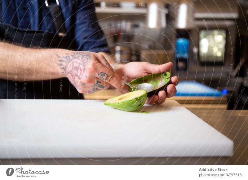 Unrecognizable chef peeling avocado in kitchen man vegetable cook recipe culinary cuisine ingredient cutting board prepare green spoon male fresh process tattoo