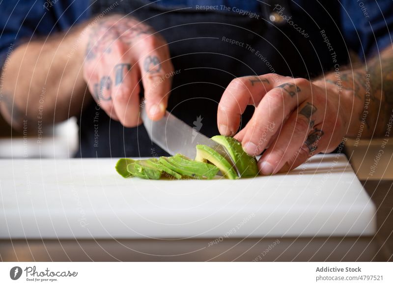 Anonymous concentrated chef cutting ripe avocado man vegetable kitchen cook culinary cuisine ingredient product food prepare cutting board male fresh tattoo