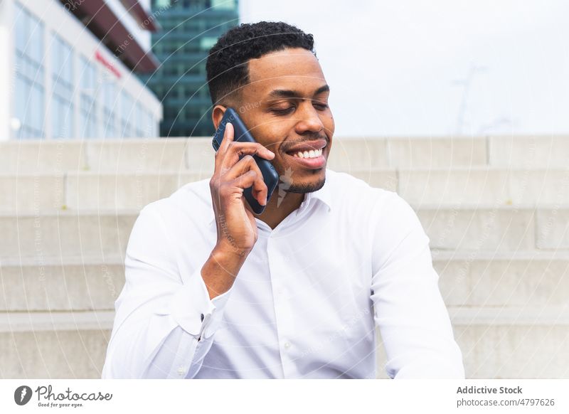 Cheerful black businessman talking on smartphone on street entrepreneur urban city chat phone call conversation formal style modern well dressed staircase