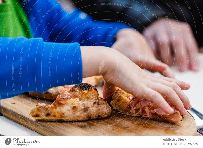 Crop child eating pizza in restaurant piece table street delicious tradition lunch kid portion junk food crust burn lumber timber wooden board yummy slice