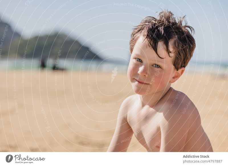 Happy boy on sandy beach looking at camera kid summer coast childhood rest pastime sea having fun positive smile happy content shore recreation naked torso