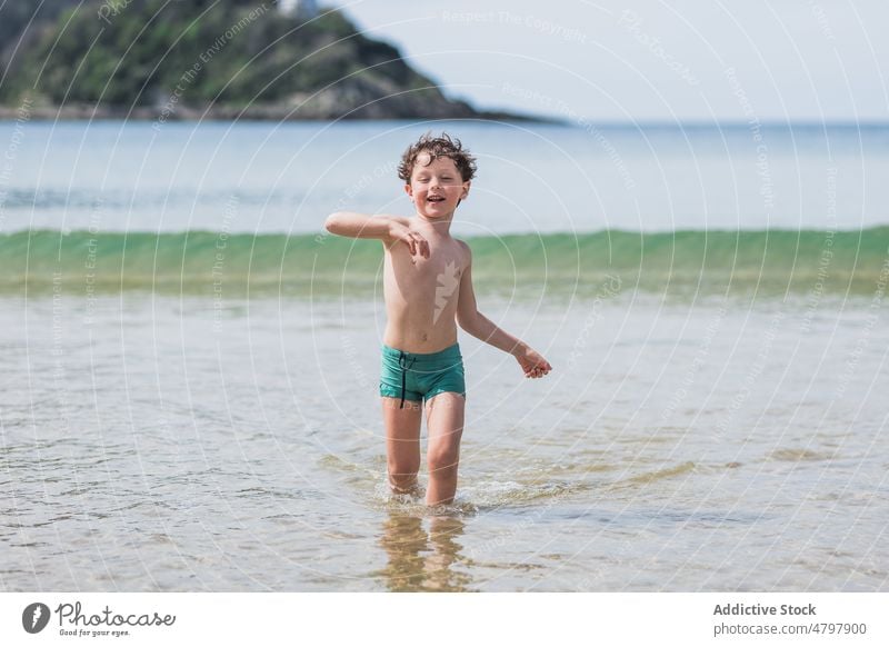 Happy boy running on sea kid beach summer smile coast childhood rest cheerful carefree glad pastime delight shore recreation naked torso shirtless water wave