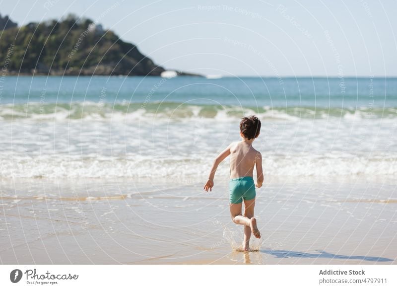 Unrecognizable boy running towards sea kid beach summer coast childhood rest carefree pastime shore recreation naked torso shirtless water wave activity active