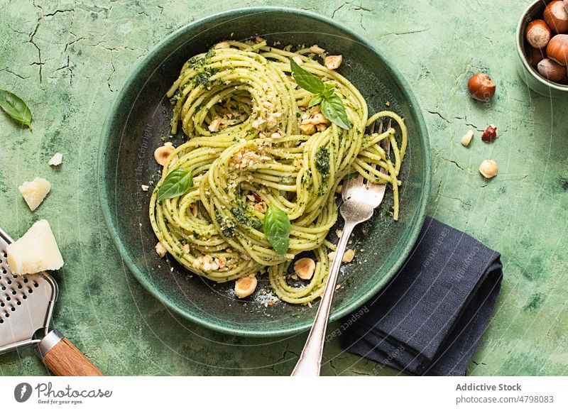 Ceramic plate with hazelnut pesto spaghetti on green table surface bowl rustic dinner culinary basil leaves napkin tagliatelle italy pesto sauce ceramic