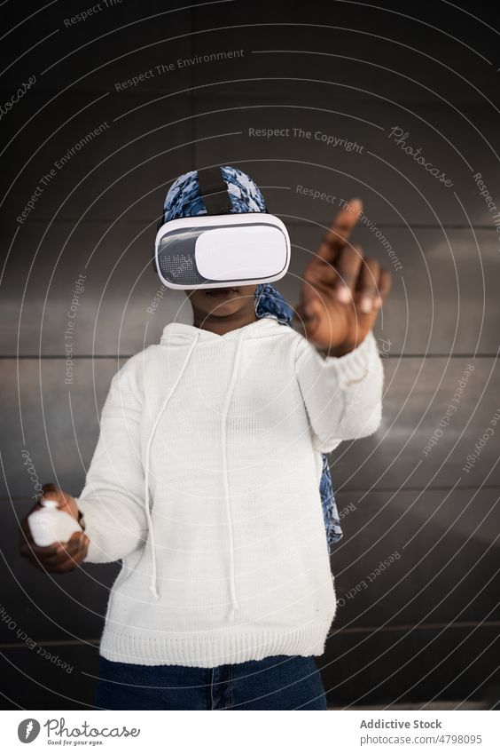 Young black lady exploring cyberspace in VR goggles woman virtual reality controller experience vr play push headscarf headset using concentrate focus digital