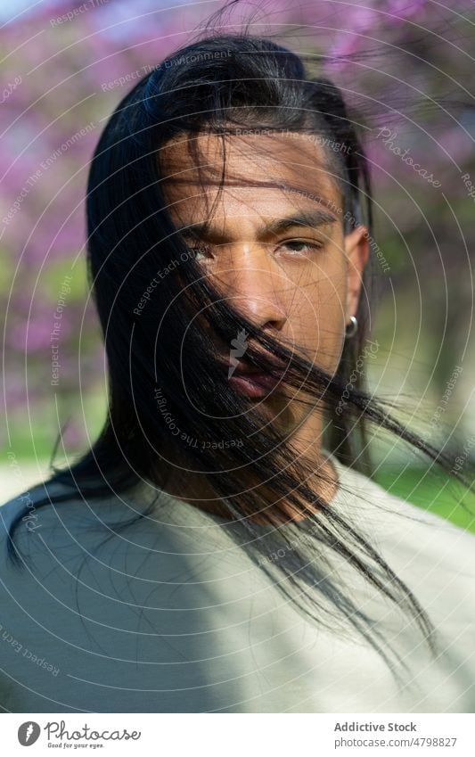 Hispanic man standing in park appearance style trendy street shadow summer sunshine handsome long hair hispanic male calm young serious guy stare sunlight