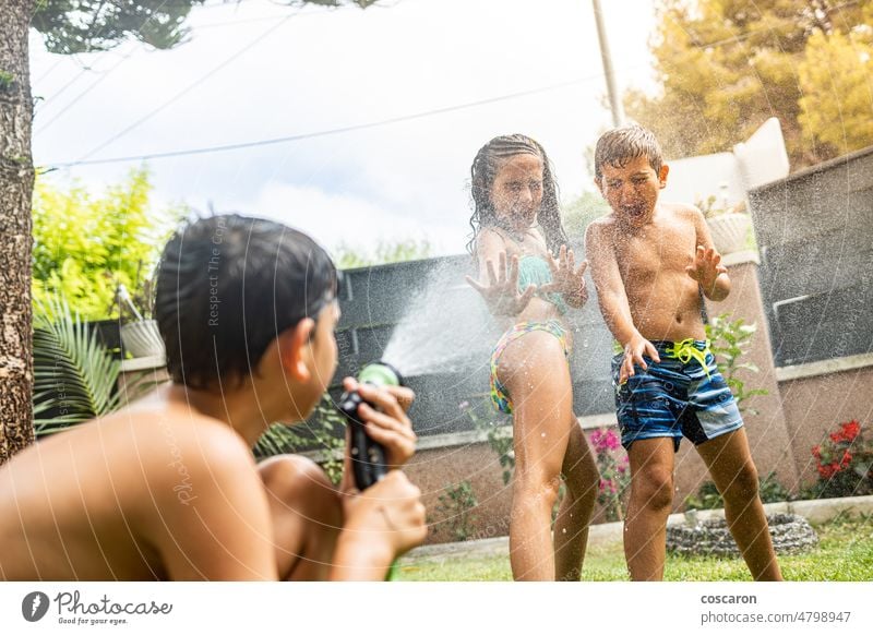Three funny kids playing with a hose in the garden active activity boy child childhood children drop drops enjoy family fountain friends friendship game girl