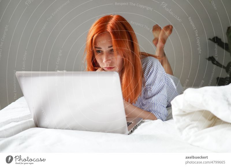 young woman lying on bed with laptop computer relax at home watching streaming movie video chat webcam bedroom real people entertainment communication work