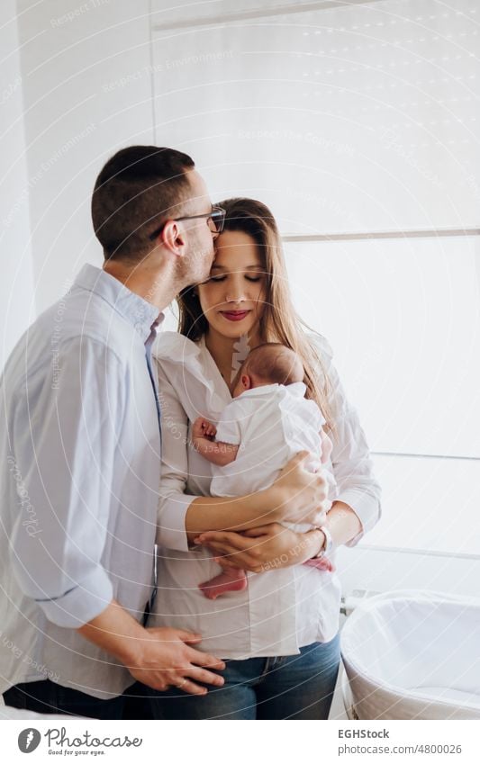 Dad kissing mother. Mom holding newborn baby. Happy family. Mother, father and son dad mom mum daddy happy parent kid together togetherness indoor infant