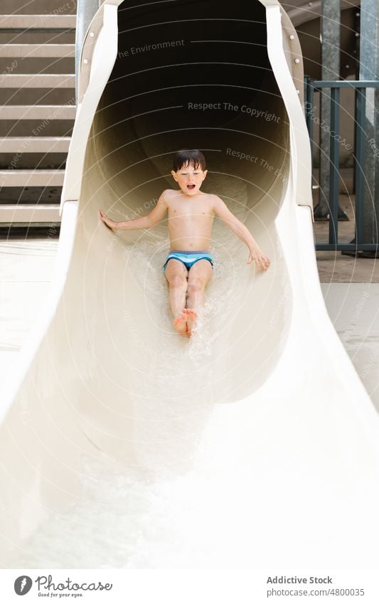 Cute child riding slide in water park on sunny summer day boy ride entertain aqua excited activity childhood joy having fun motion kid wet hair dark hair
