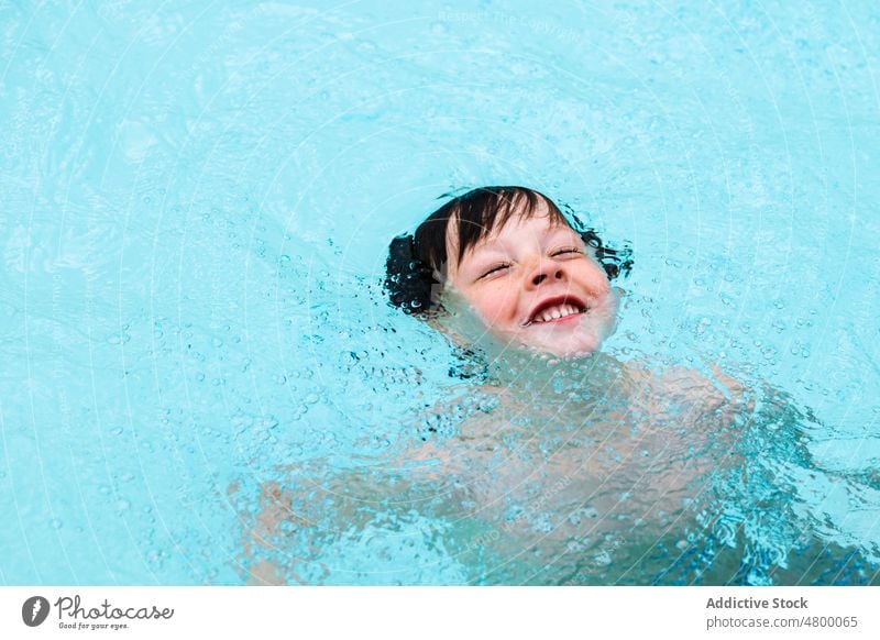 Adorable child swimming in pool on sunny day summer holiday childhood activity enjoy boy water vacation resort cute kid wet hair dark hair leisure wellness