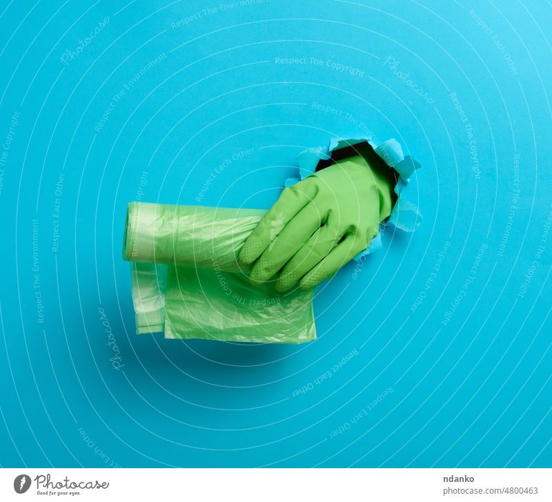 hand holds a bundle of transparent garbage bags on a blue background. A part of the body sticks out of a torn hole in the paper glove green arm bin blank can