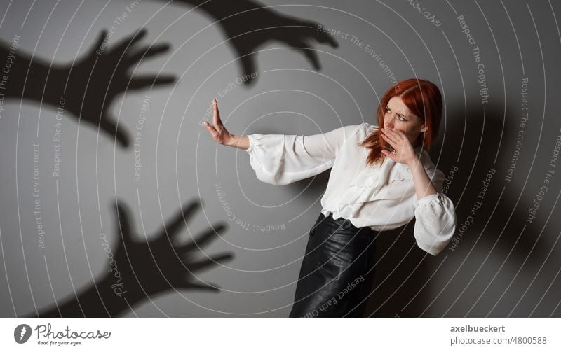 terrified woman in defensive posture is attacked by shadows of hands sexual harassment fear assault abuse violence grab person female problem bully emotion