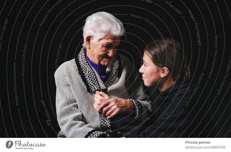 Elderly woman sitting with an adult granddaughter a black background. 80s care pensioner mother's day grandmother family together beautiful beauty caucasian
