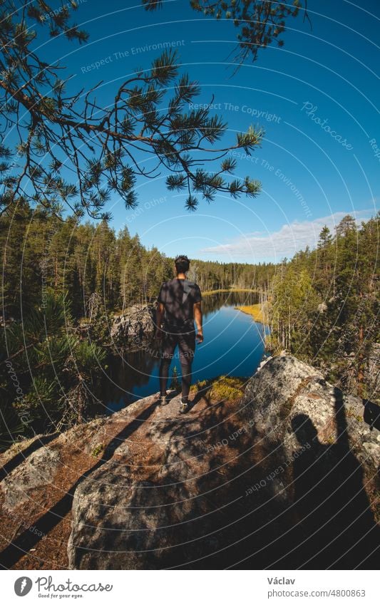 traveller aged 24 is lying on a high rock and observing a beautiful natural lake in hiidenportti National Park, Sotkamo in kainuu region, Finland. Hiking the Finnish countryside